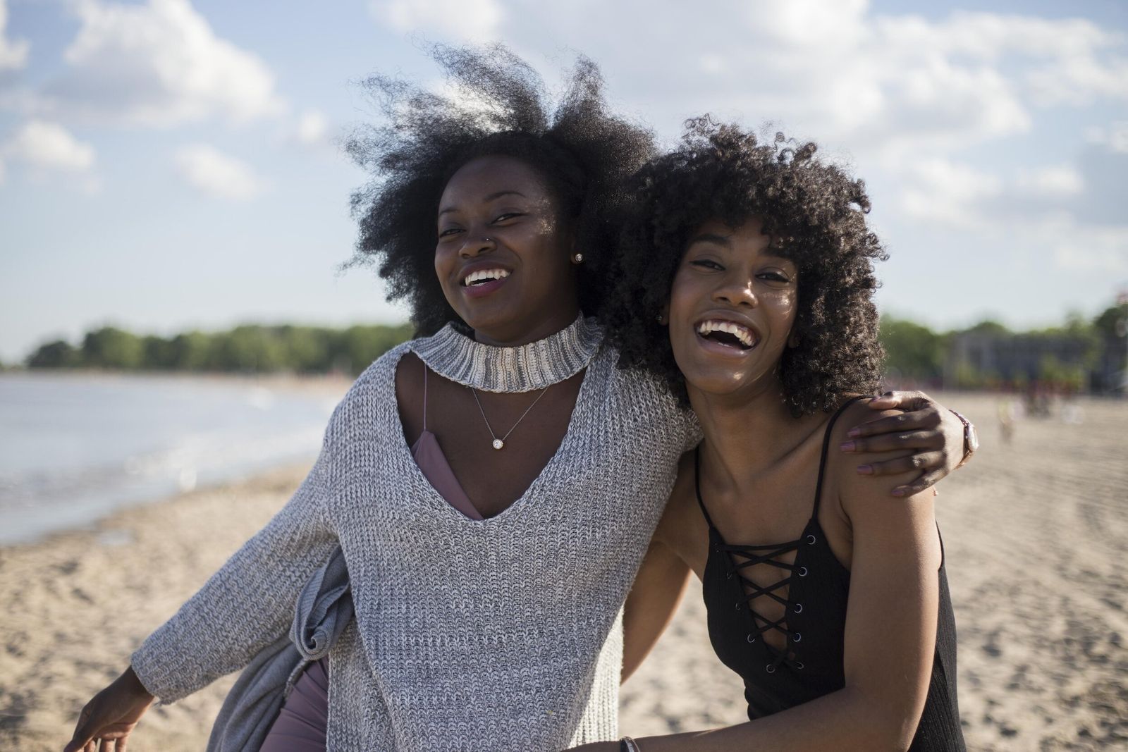 Two smiling Black women embracing on a sunny Toronto beach