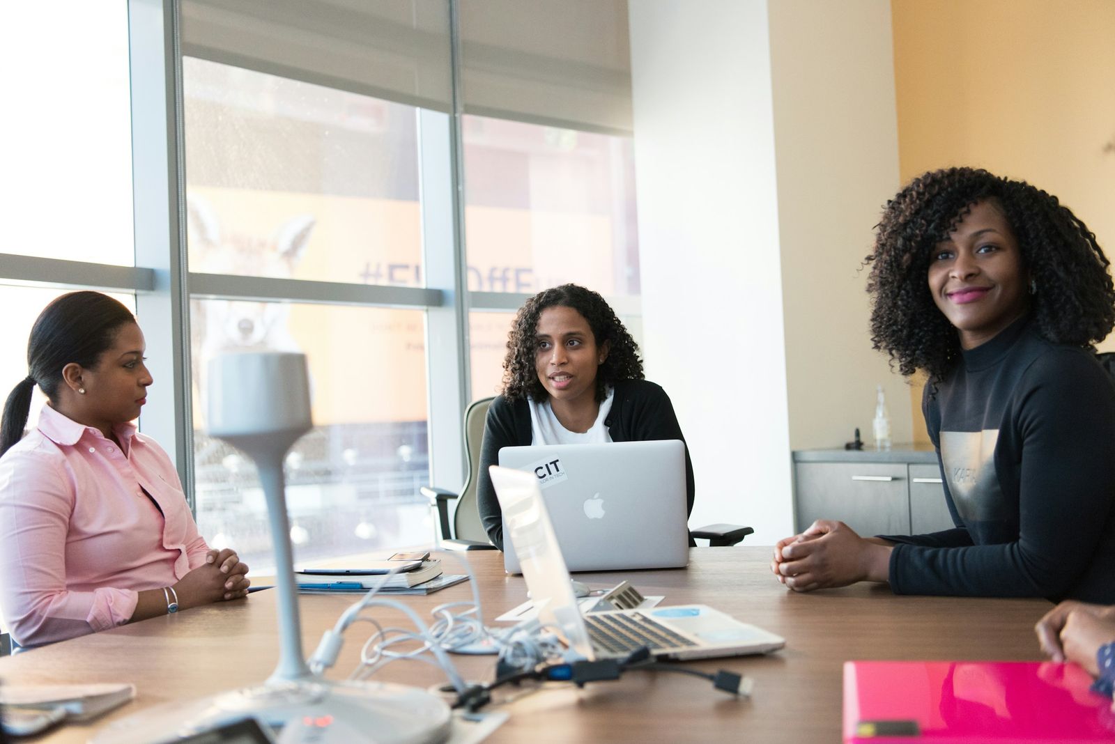 Three colleagues in conversation at a table with a laptop